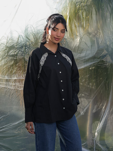 Woman wearing a black shirt with white embroidery standing against a transparent backdrop.