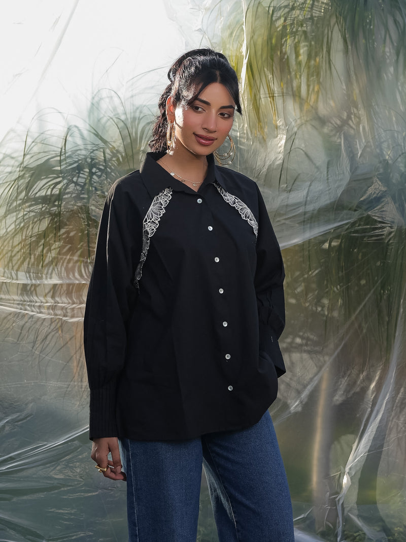 Woman wearing a black shirt with white embroidery standing against a transparent backdrop.