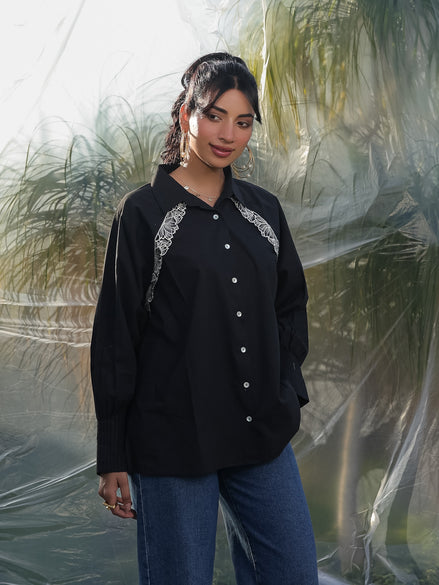 Woman wearing a black shirt with white embroidery standing against a transparent backdrop.