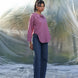 Woman in a mauve pink shirt and blue jeans standing on a beach with palm trees in the background