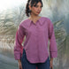 Woman wearing a pink shirt and blue jeans standing against a textured white background