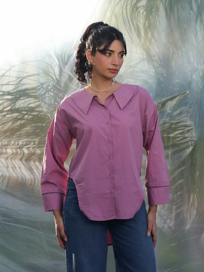 Woman wearing a pink shirt and blue jeans standing against a textured white background
