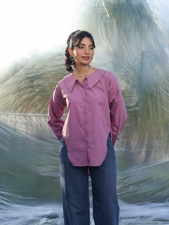 Woman wearing a pink stylish shirt and blue jeans standing against a textured white background