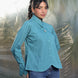 Woman wearing a teal blue shirt and blue jeans standing against a blurred natural background