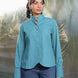 Woman wearing a teal cotton shirt and blue jeans standing against a textured white background