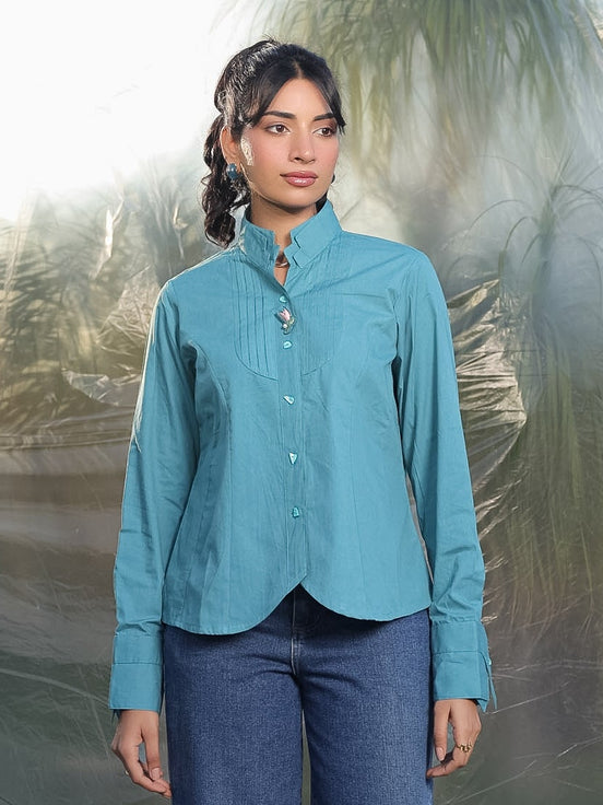 Woman wearing a teal cotton shirt and blue jeans standing against a textured white background