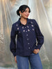 Woman wearing a navy blue embroidered shirt with a plain background