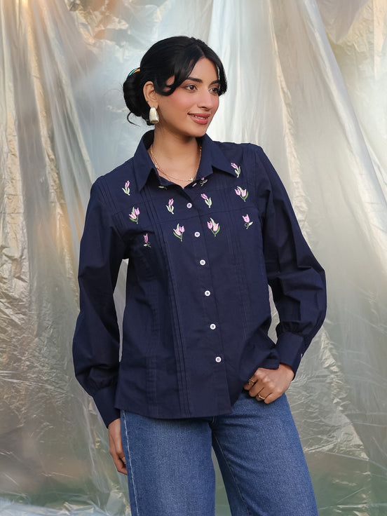 Woman wearing a navy blue embroidered shirt with a plain background