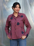 Woman wearing a purple shirt with dark blue tulip applique patches against a plain background