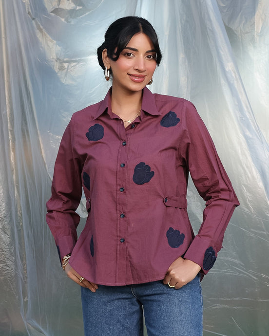 Woman wearing a purple shirt with dark blue tulip applique patches against a plain background