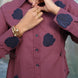 Person wearing a plum shirt with navy blue patches, accessorized with gold jewelry.