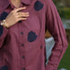 Person wearing a purple pink shirt with navy appliqués, standing outdoors.
