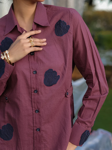 Person wearing a purple pink shirt with navy appliqués, standing outdoors.