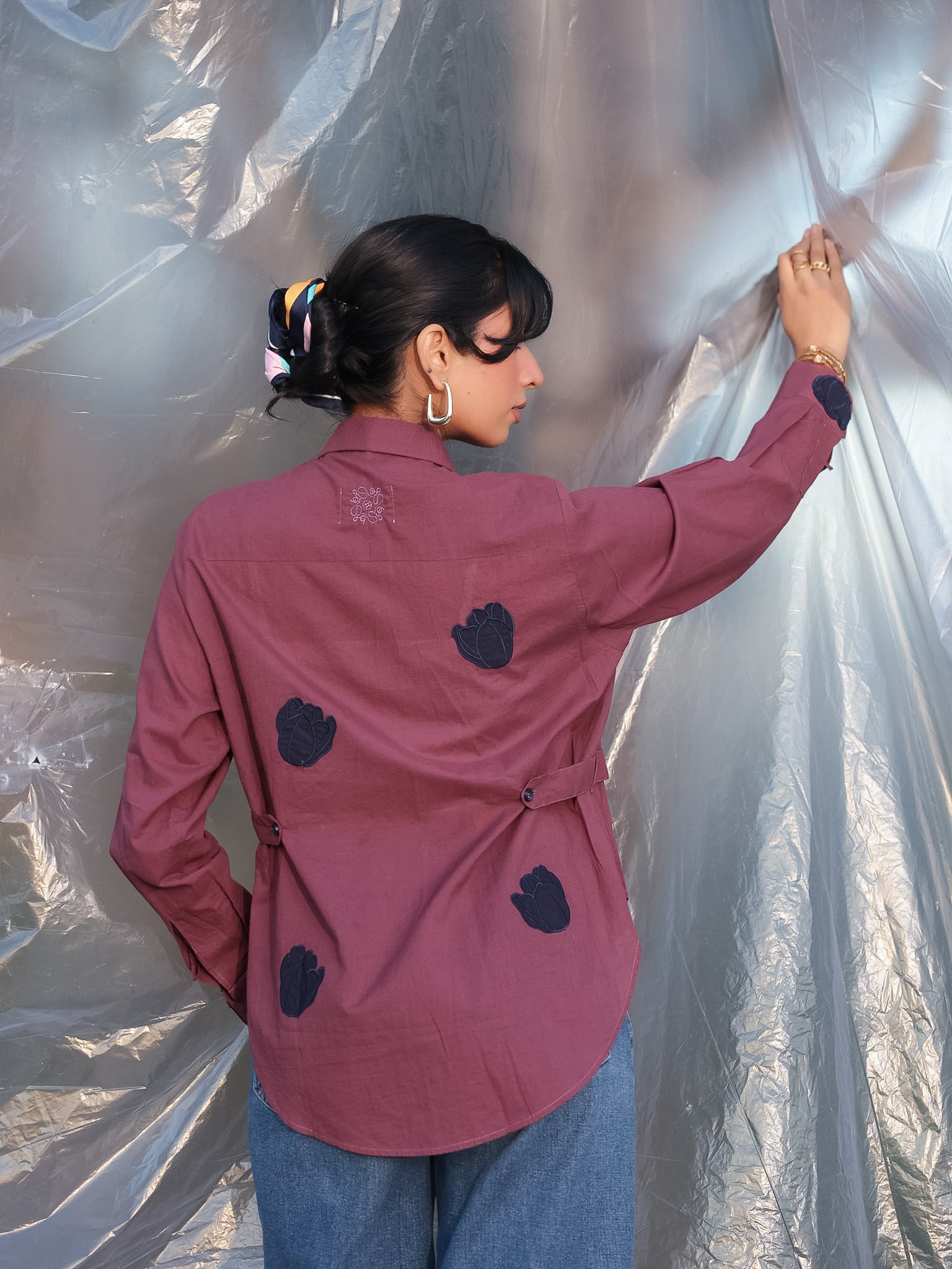 Person wearing a plum shirt with aesthetic navy blue tulip embroidered applique on the shirt against a silver tarp background