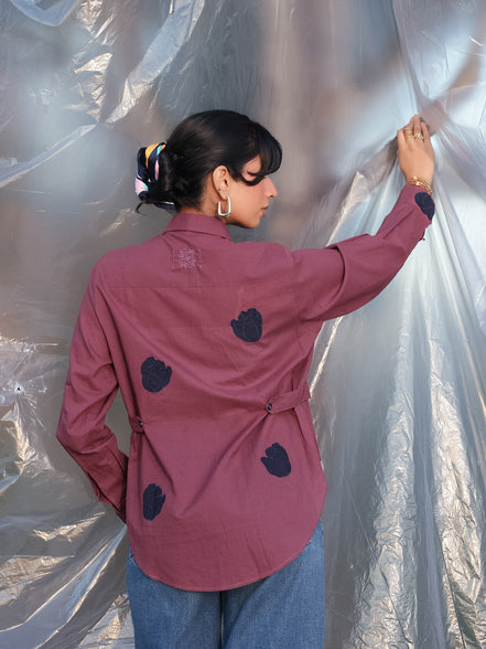 Person wearing a plum shirt with aesthetic navy blue tulip embroidered applique on the shirt against a silver tarp background
