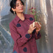 Woman wearing a maroon shirt with navy blue tulip appliques, holding flowers against a textured white background.