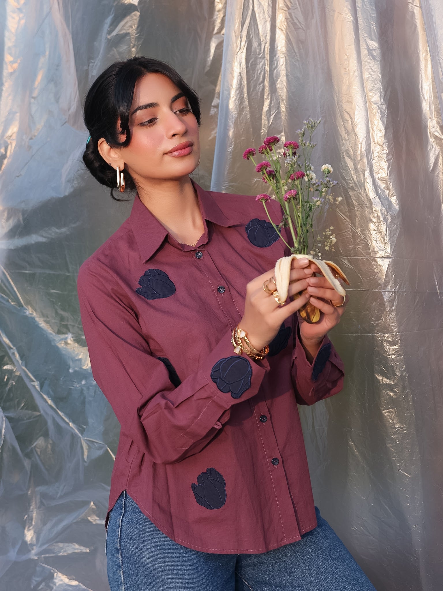Woman wearing a maroon shirt with navy blue tulip appliques, holding flowers against a textured white background.