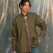 Woman wearing a olive green shirt with pink accents against a plain background