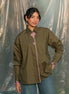 Woman wearing a olive green shirt with pink accents against a plain background