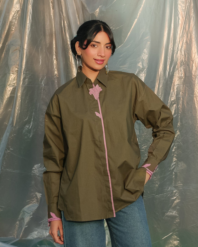 Woman wearing a olive green shirt with pink accents against a plain background