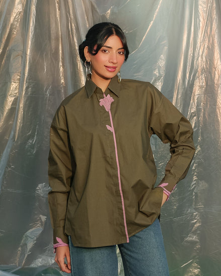 Woman wearing a olive green shirt with pink accents against a plain background