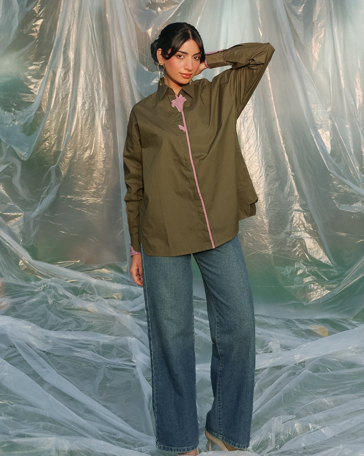Woman wearing an olive green shirt and blue jeans standing behind a plastic sheet