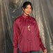 Person wearing a maroon shirt with a tie and blue jeans standing against a tarp background