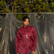 Person wearing a maroon wine silk chanderi shirt with a designer tie, standing against a backdrop of green foliage and plastic sheeting.