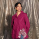 Woman wearing a pink shirt with stylish floral embroidery and blue jeans standing against a plastic sheet background