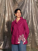 Woman wearing a pink shirt with stylish floral embroidery and blue jeans standing against a plastic sheet background