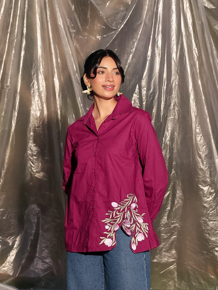 Woman wearing a pink shirt with stylish floral embroidery and blue jeans standing against a plastic sheet background