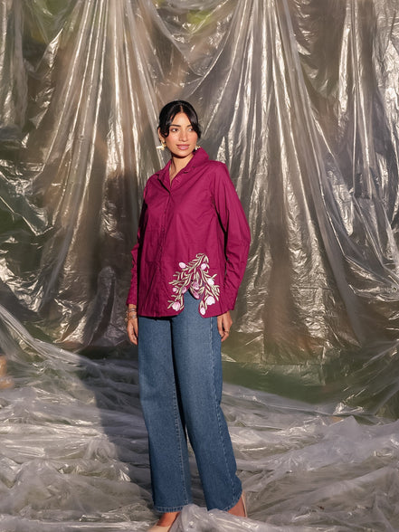 Person wearing a maroon wine shirt with floral embroidery and blue jeans standing inside a large plastic sheet.