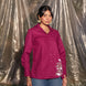 Woman wearing a magenta shirt with floral embroidery against a reflective silver curtain.